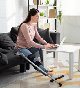 Person with leg brace and crutch using a laptop