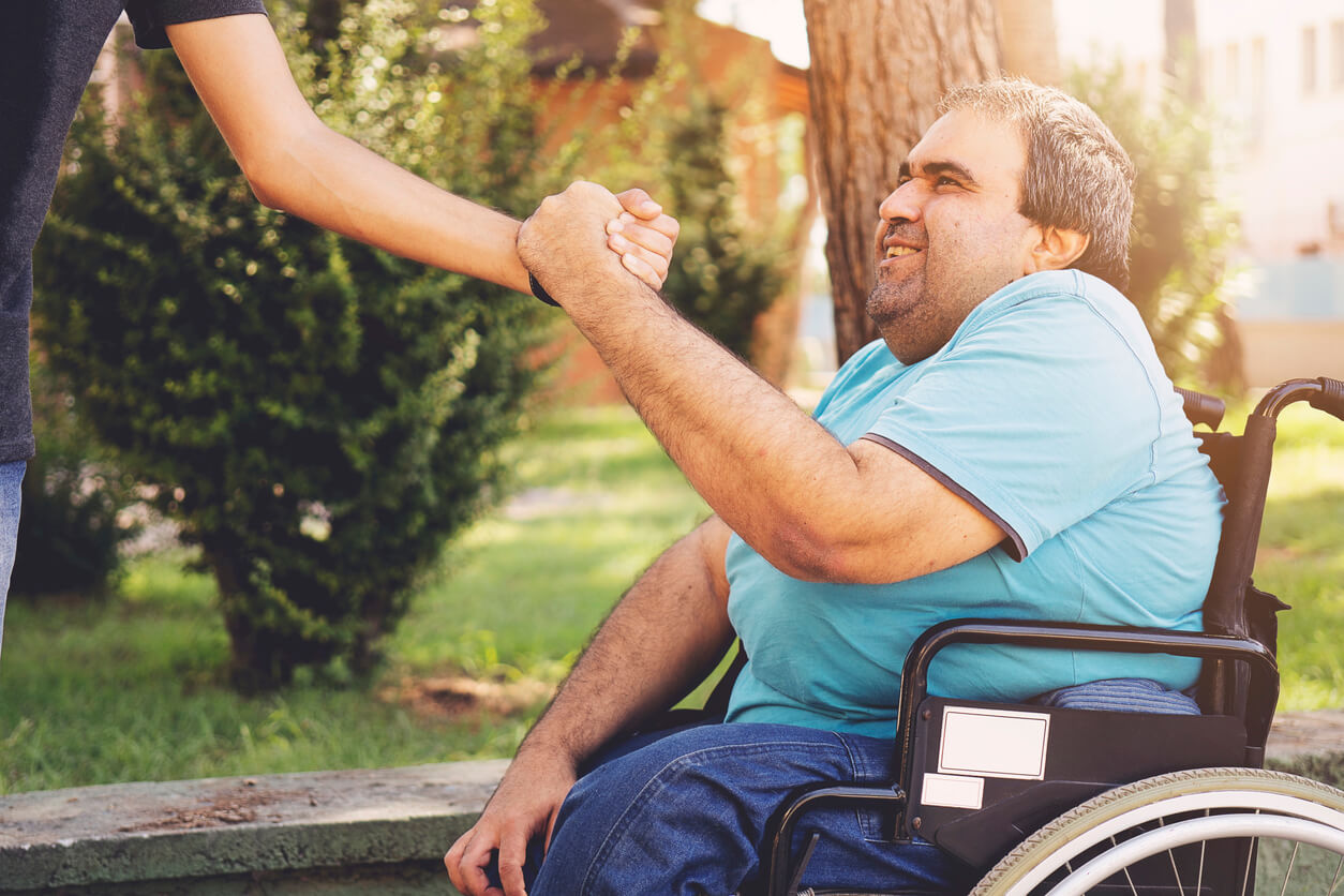 man in wheel chair holding persons hand