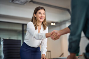 Happy mid aged lawyer woman handshaking greeting client in office.