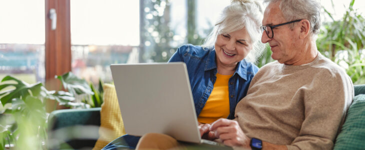 Senior couple using laptop while sitting on sofa in living room at home