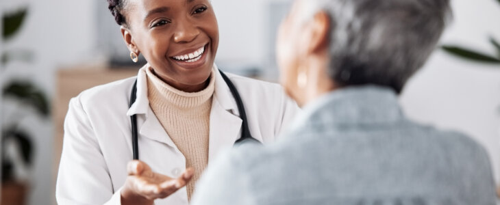 Smile, black woman or doctor consulting a patient in meeting in hospital for healthcare feedback or support. Happy, medical or nurse with a mature person talking or speaking of test results or advice