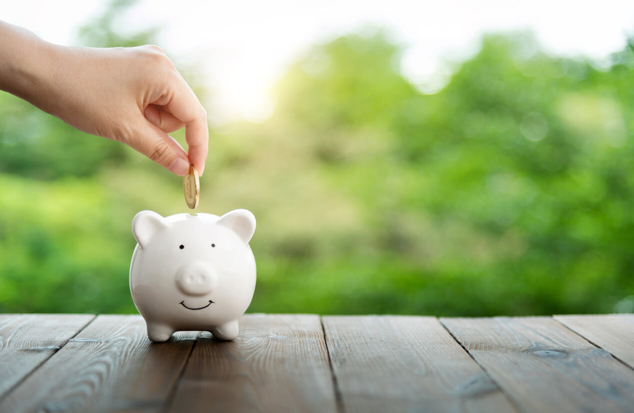 Human hand putting coin into piggy bank